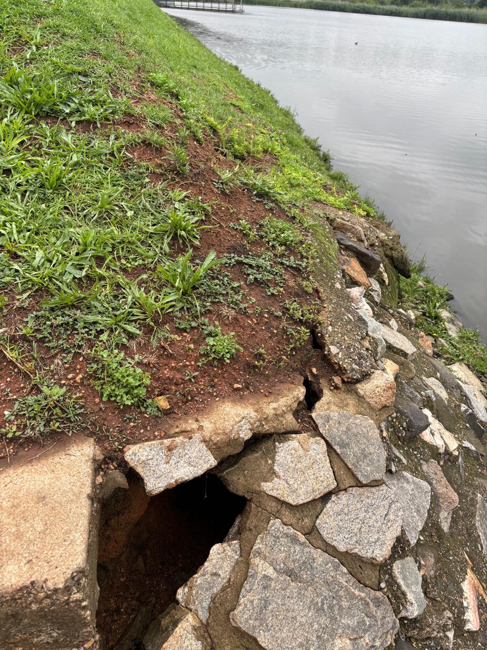 Collapsed cavity at the edge of a dam wall with a dark void opening beneath the stonework