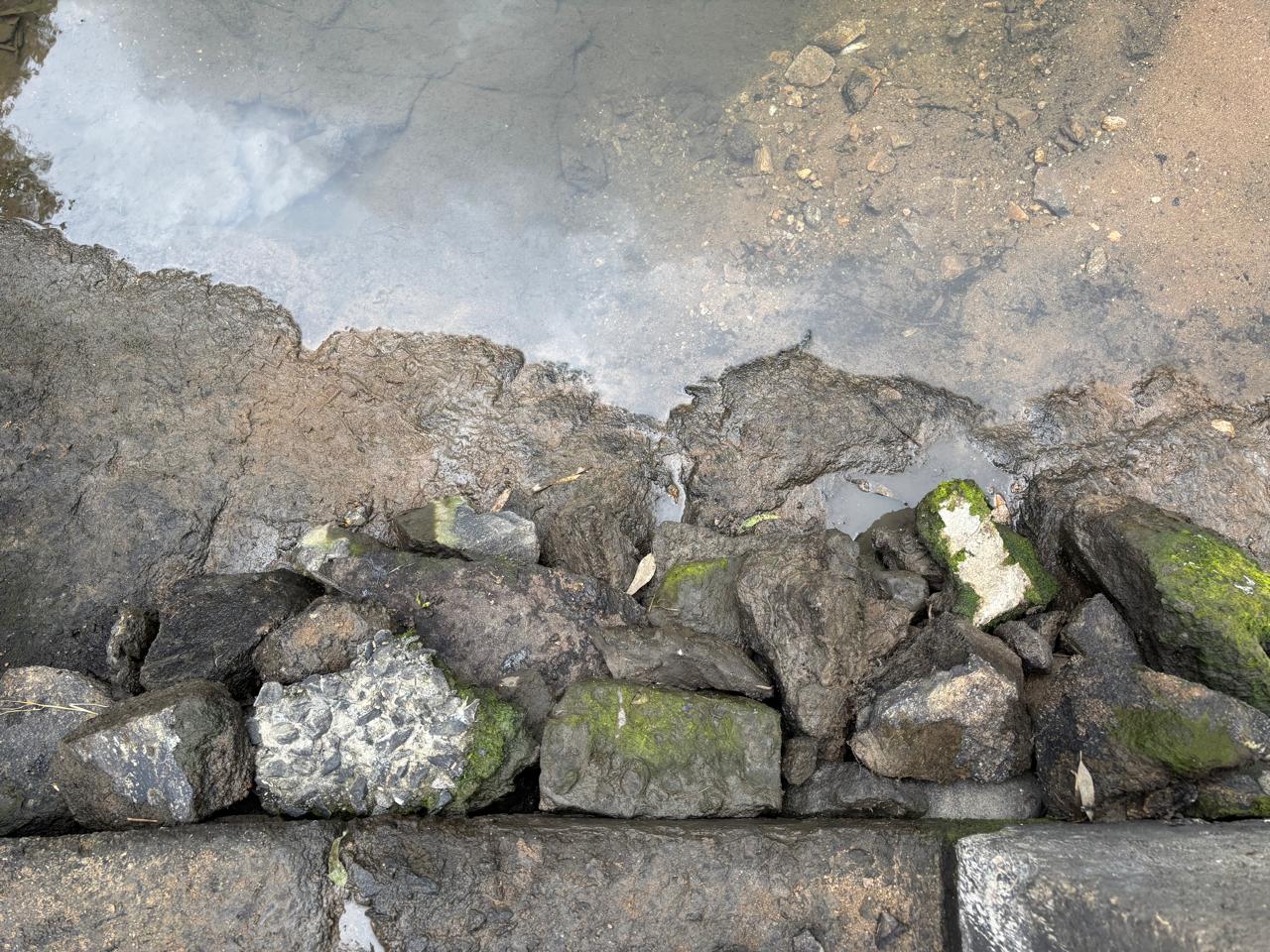Eroded base of the spillway with loose rock exposed at the water edge